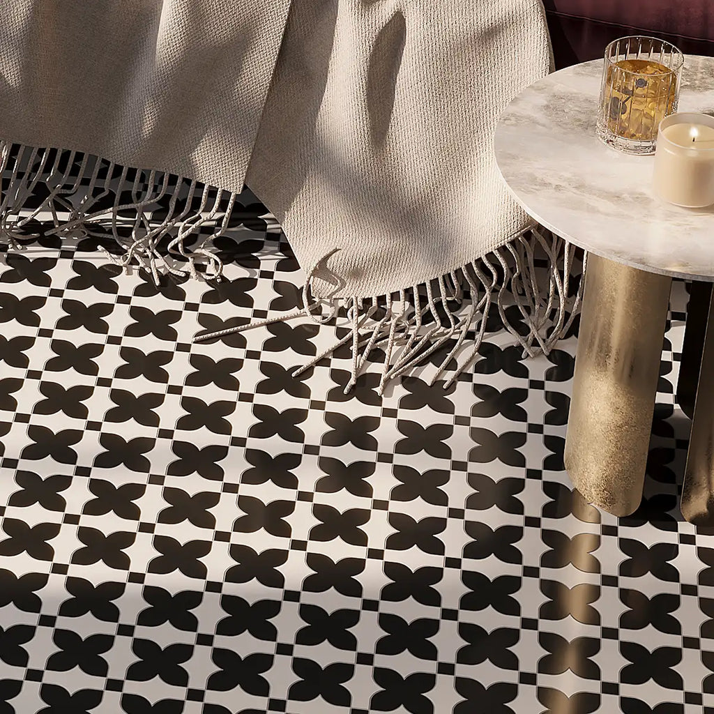 Black and white geometric patterned marble floor tiles styled in a modern interior setting with a cream fringed throw blanket and a marble-topped side table.