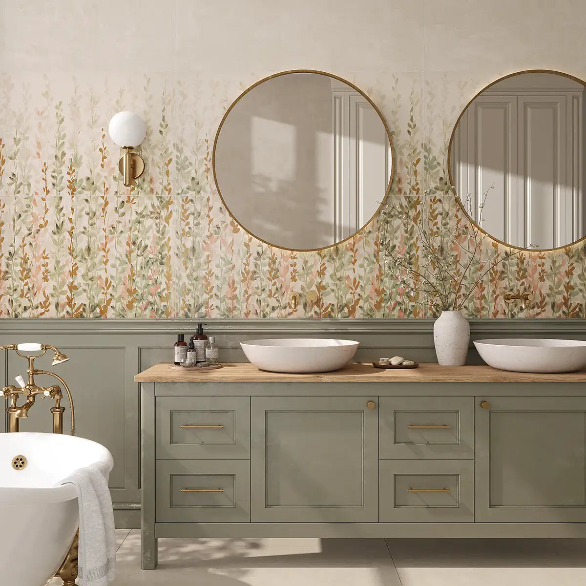 A styled bathroom interior featuring a sage green double-sink vanity with a light wood countertop, two white vessel sinks, round gold-framed mirrors, and a floral patterned porcelain tile backsplash wall.