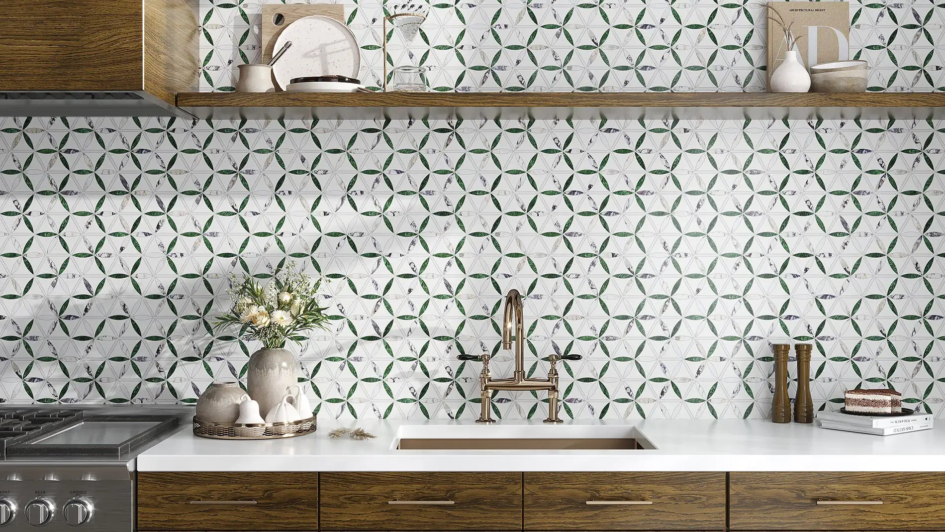 A kitchen backsplash featuring white mosaic tiles with a green geometric pattern, installed behind a white countertop, a brass faucet, and dark wood cabinets.