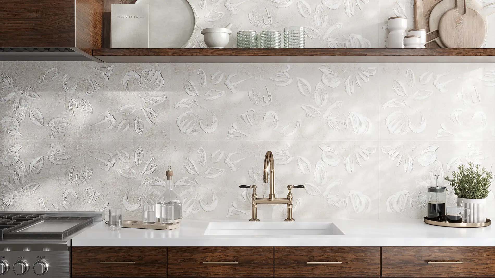 A modern kitchen backsplash featuring white textured ceramic tiles with a raised floral pattern, paired with dark wood cabinets and a gold faucet.